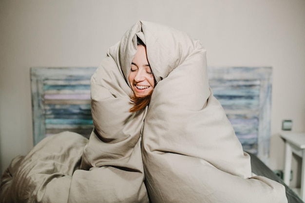 Mujer sonriente con una manta sentada en la cama en casa