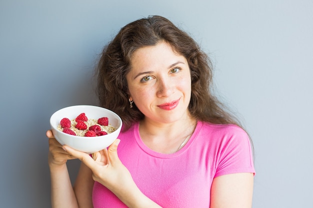 Mujer sonriente mantenga desayuno saludable y natural, avena y frambuesas en un bol.