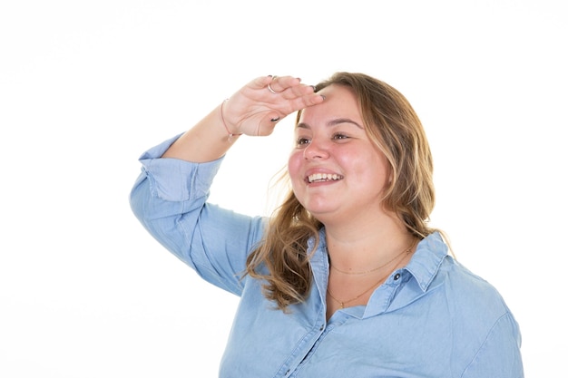 Mujer sonriente mirando a lo lejos con la mano sobre la frente hermosa atractiva joven rubia de talla grande cuerpo positivo chica 20 años aislada en el retrato de estudio de fondo de pared blanca