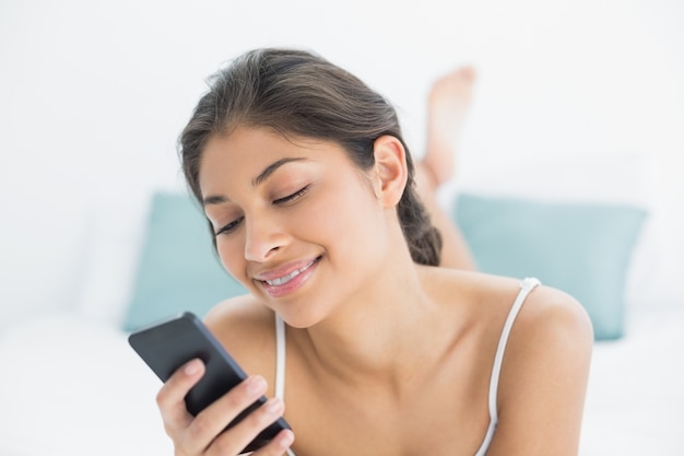 Mujer sonriente mirando el teléfono móvil en la cama