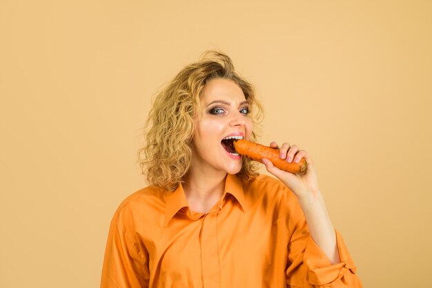 Mujer sonriente muerde zanahoria vegetal que tiene un buen impacto en los dientes, alimentación saludable, dieta vegetariana.