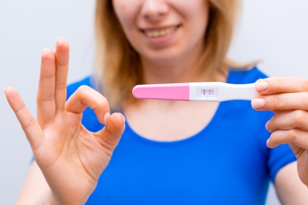 La mujer sonriente muestra el signo ok y tiene una prueba de embarazo positiva