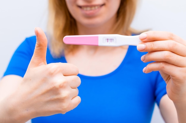 Mujer sonriente muestra signos como y sosteniendo una prueba de embarazo positiva