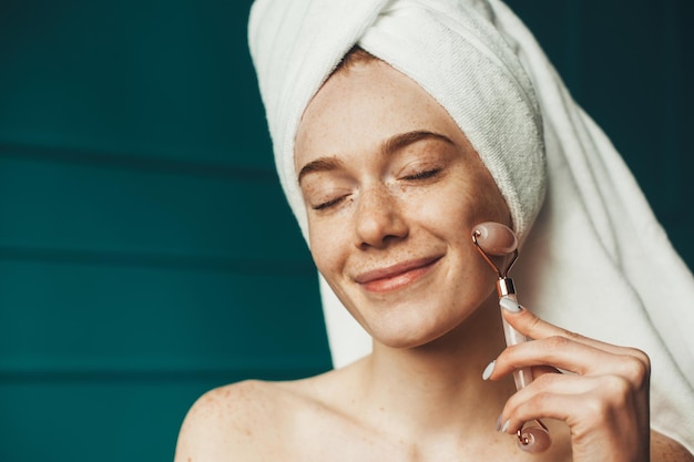 Mujer sonriente con los ojos cerrados con rodillo facial de jade para el cuidado de la piel hermoso retrato natural sto