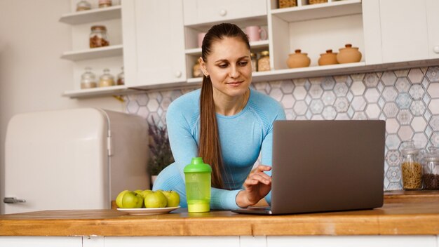 Foto mujer sonriente con ordenador en el interior de la cocina moderna. concepto de estilo de vida saludable y cocina. una mujer está buscando una receta o está transmitiendo en línea