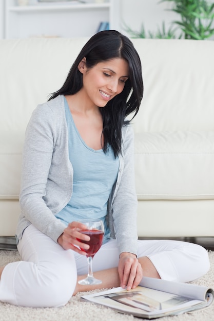 Mujer sonriente pasar las páginas de una revista mientras sostiene un vaso de vino tinto