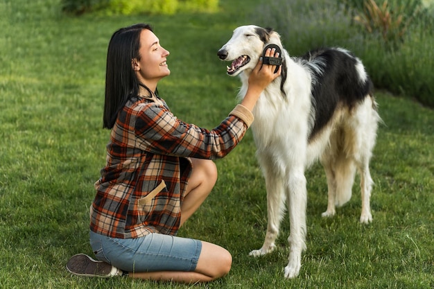 Mujer sonriente peina a su perro de raza lobo ruso en la foto de la calle en plena estatura