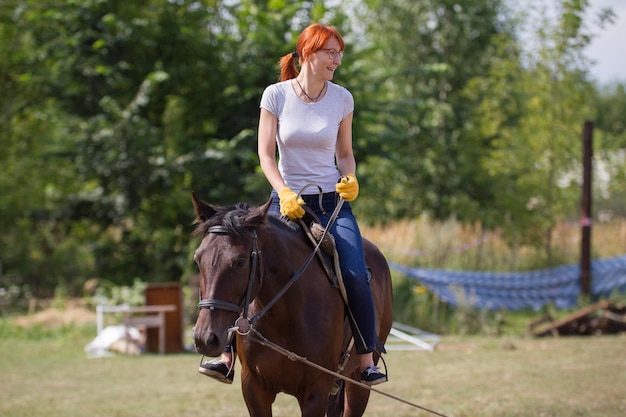 Una mujer sonriente pelirroja montando un caballo en el campo