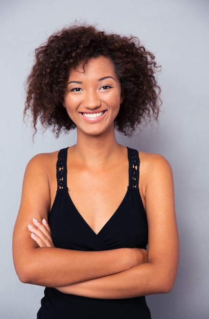 Mujer sonriente de pie con los brazos cruzados sobre la pared gris