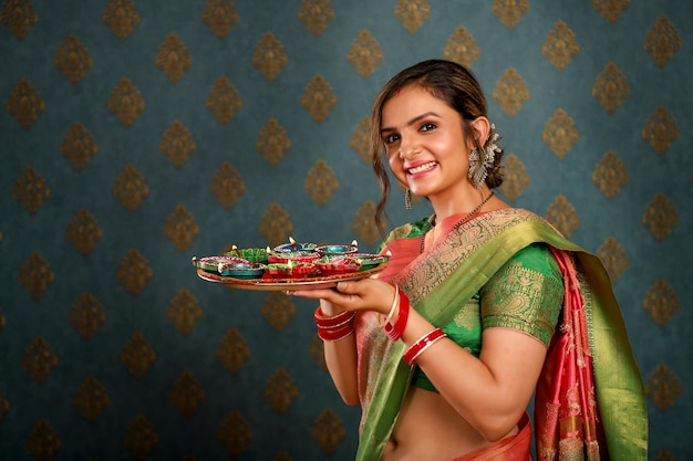 Foto una mujer sonriente de pie con un sari y sosteniendo un plato de pooja en una foto tomada durante el diwa