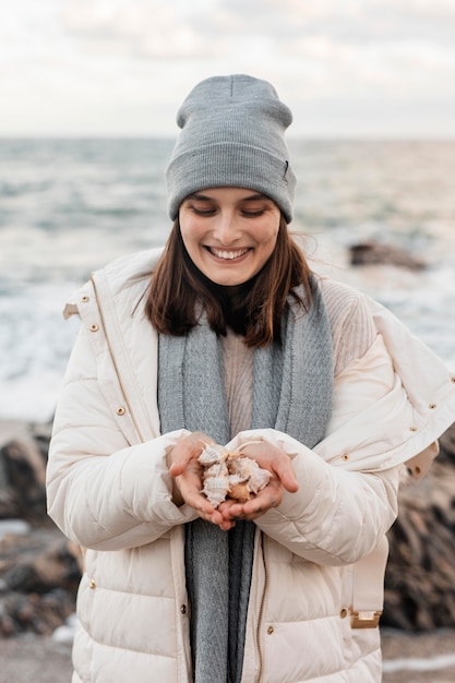 Mujer sonriente en la playa sosteniendo conchas marinas