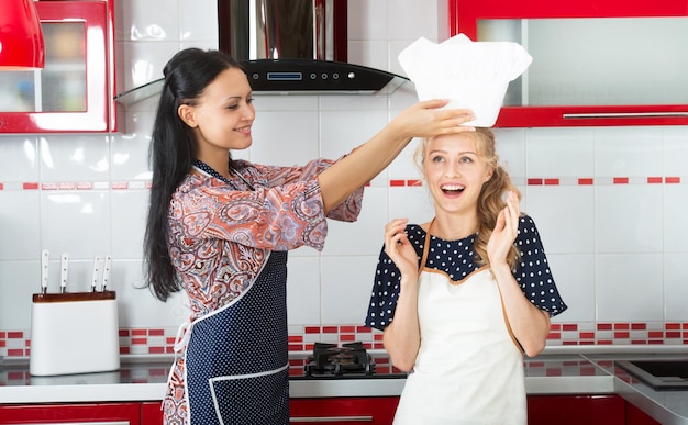 Mujer sonriente poniendo un sombrero de chef en la cabeza de su amiga más joven