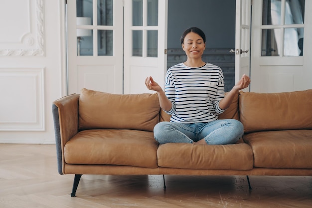 Mujer sonriente practicando yoga medita sentada en un sofá en casa Bienestar de estilo de vida saludable