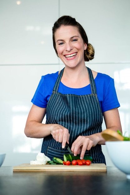 Mujer sonriente preparando verduras para la cena en una tabla de cortar de madera