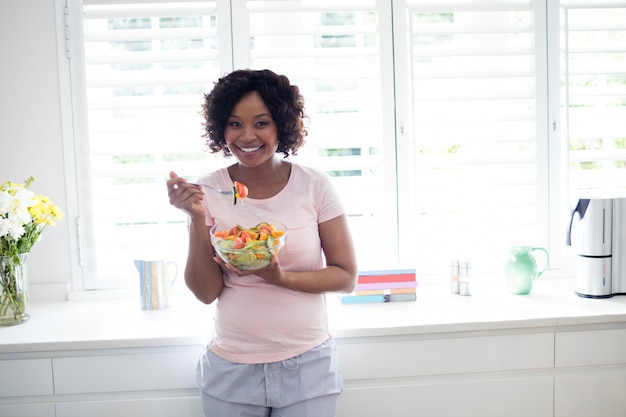 Mujer sonriente que come la ensalada en cocina