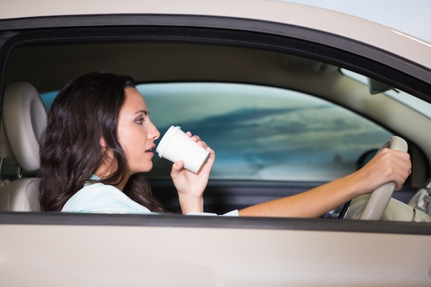 Mujer sonriente que conduce el coche mientras bebe café