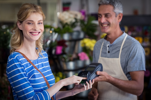 Mujer sonriente que hace el pago con su tarjeta de crédito a floristería