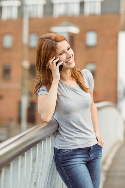 Mujer sonriente que se inclina en el puente que hace una llamada telefónica