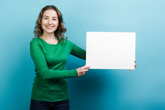 Mujer sonriente que lleva a cabo el cartel blanco en blanco