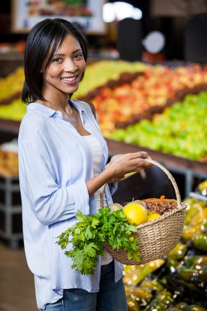 Mujer sonriente que sostiene frutas y verduras en cesta