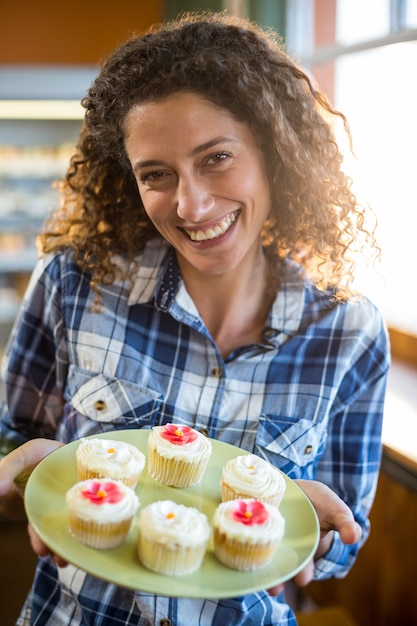 Foto mujer sonriente que sostiene la placa de la torta de la taza en supermercado