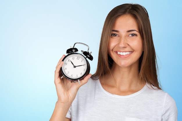 Mujer sonriente que sostiene el reloj de la alarma