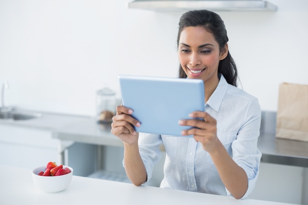 Mujer sonriente que sostiene su tableta que se coloca en cocina brillante