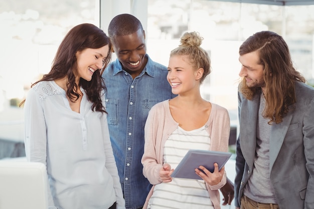 Mujer sonriente que sostiene la tableta digital y que discute con los compañeros de trabajo