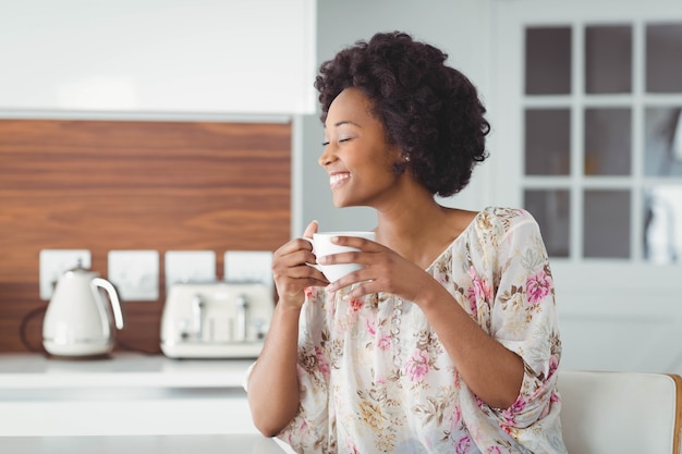 Mujer sonriente que sostiene la taza blanca en la cocina