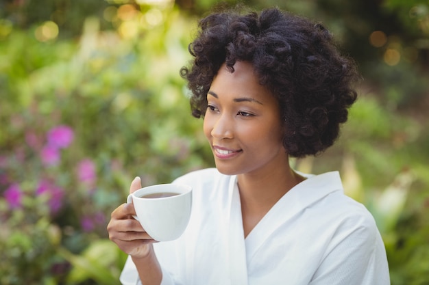 Mujer sonriente que sostiene la taza en el jardín