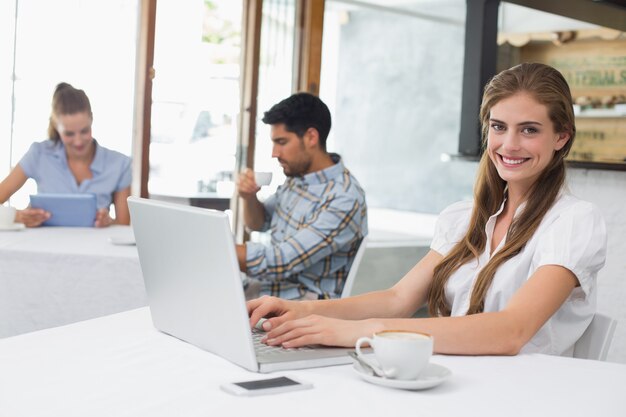 Mujer sonriente que usa la computadora portátil en cafetería