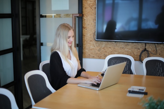 Una mujer sonriente que usa una computadora portátil en el lugar de trabajo para pequeñas empresas que buscan involucrar al público y la creación de contenido a escala puede adoptar nuevas tecnologías de marketing en el espacio de trabajo. Concepto de autónomo.