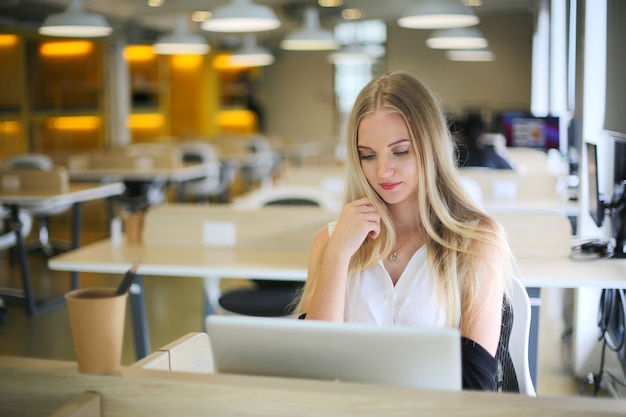 Una mujer sonriente que usa una computadora portátil en el lugar de trabajo para pequeñas empresas que buscan involucrar al público y la creación de contenido a escala puede adoptar nuevas tecnologías de marketing en el espacio de trabajo. Concepto de autónomo.