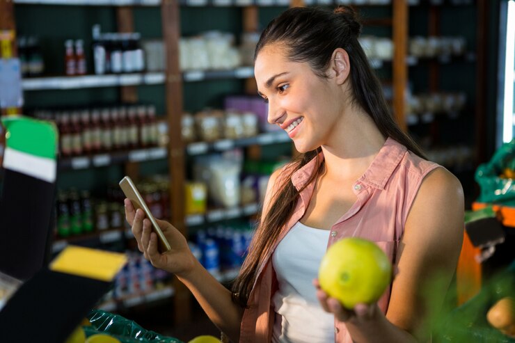Foto mujer sonriente que usa su teléfono mientras compra frutas en la sección orgánica