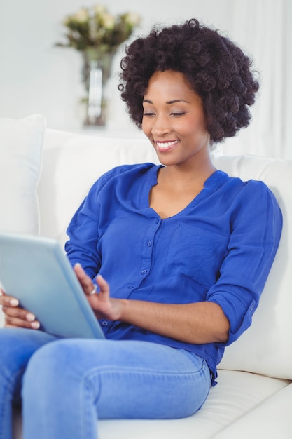 Mujer sonriente que usa la tableta en el sofá