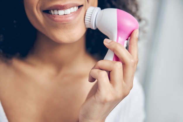 Mujer sonriente realizando un procedimiento cosmético con un cepillo de limpieza facial