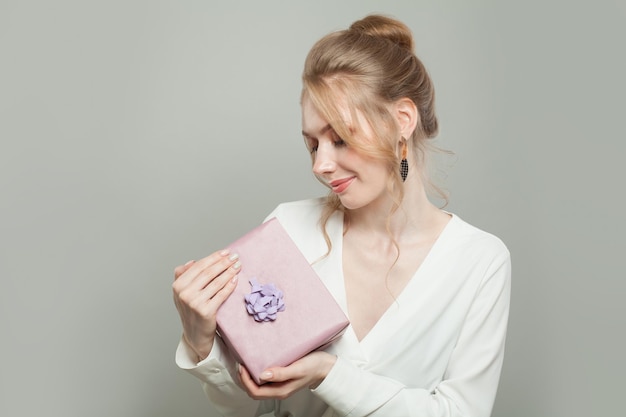 Mujer sonriente con un regalo rosado sobre un fondo gris