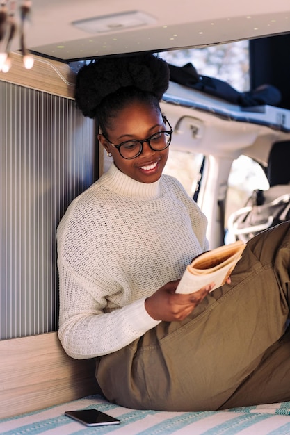 mujer sonriente, relajante, en, autocaravana, libro de lectura