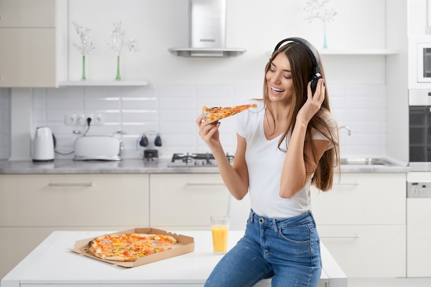 Mujer sonriente relajante con música y pizza en casa