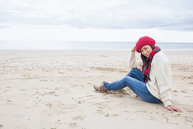 Mujer sonriente en ropa de abrigo elegante sentado en la playa