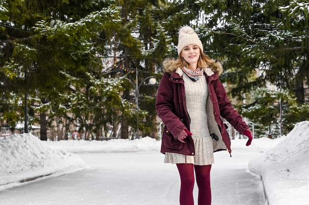 Mujer sonriente en ropa de abrigo pasar un buen rato patinaje sobre hielo en el parque de invierno cubierto de nieve. Concepto de vacaciones de invierno