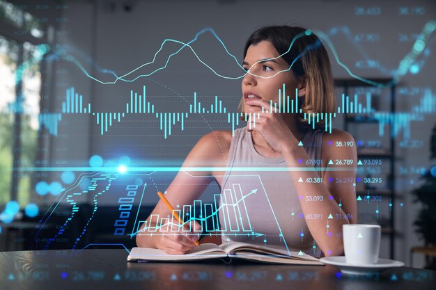 Mujer sonriente con ropa informal tomando notas en un cuaderno en el lugar de trabajo de la oficina con una taza de café Concepto de tecnología de información de educación empresarial distante soñando pensando en tablas y gráficos de Forex