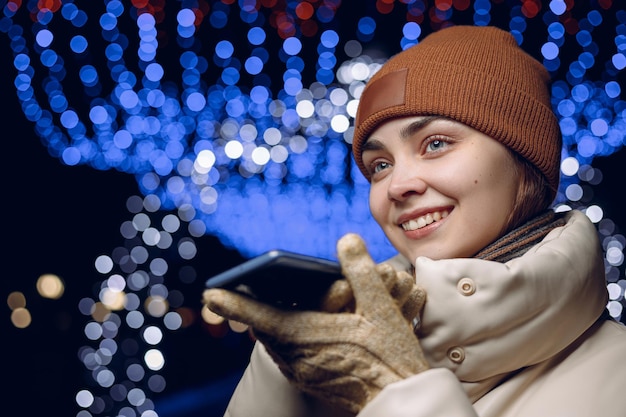 Mujer sonriente con ropa de invierno abrigada grabando mensajes de voz en las redes sociales a través de un teléfono inteligente