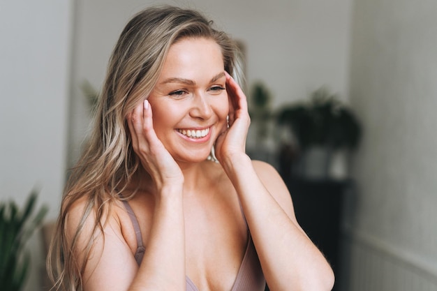 Mujer sonriente rubia de 35 años con cara limpia y fresca y manos con cabello largo hace masaje facial