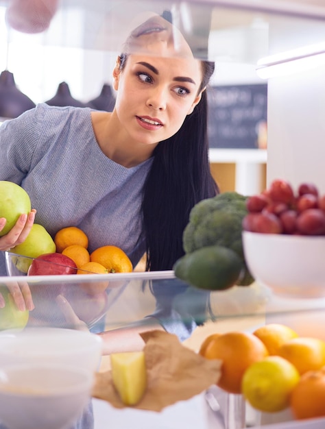 Mujer sonriente sacando una fruta fresca de la nevera concepto de comida saludable