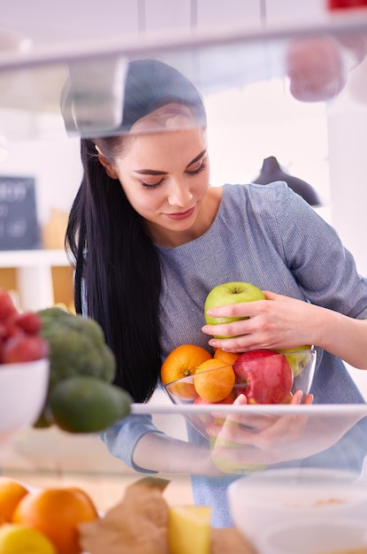 Mujer sonriente sacando una fruta fresca de la nevera concepto de comida saludable