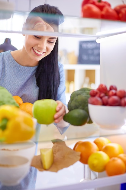 Mujer sonriente sacando una fruta fresca de la nevera concepto de comida saludable