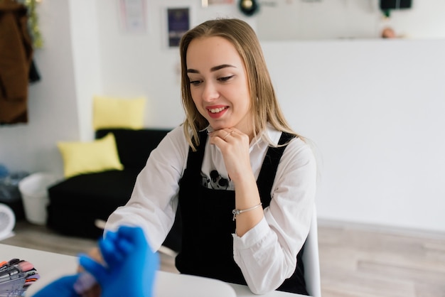 Mujer sonriente en el salón de belleza tiene una manicura del maestro de manicura. El maestro está usando una lima de uñas.