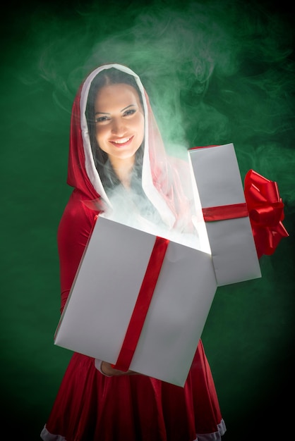 Mujer sonriente Santa abriendo la caja mágica de regalo de Navidad sobre fondo verde oscuro