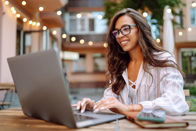 Mujer sonriente sentada en el café y trabajando en la computadora portátil Concepto de educación en línea independiente